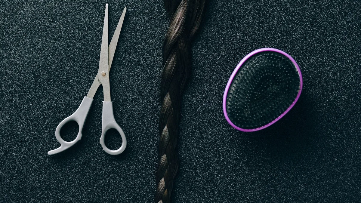 Close-up of hairdressing scissors, braided hair, and brush on black background.