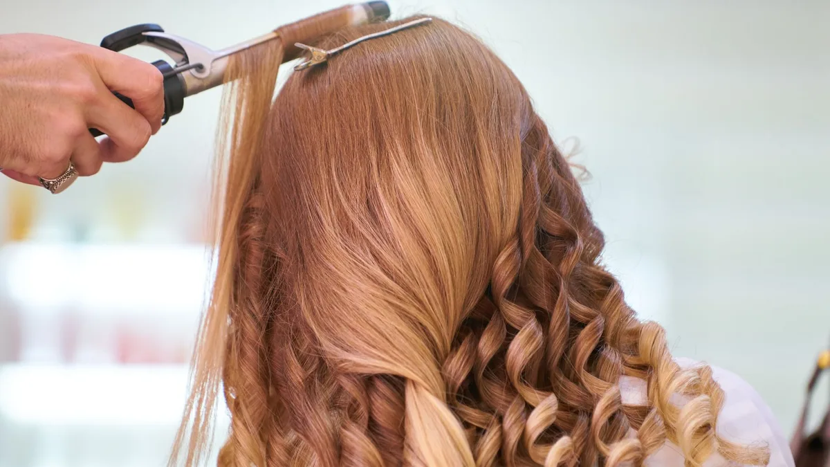 Close-up of a stylist curling blonde hair into glamorous curls at a salon.