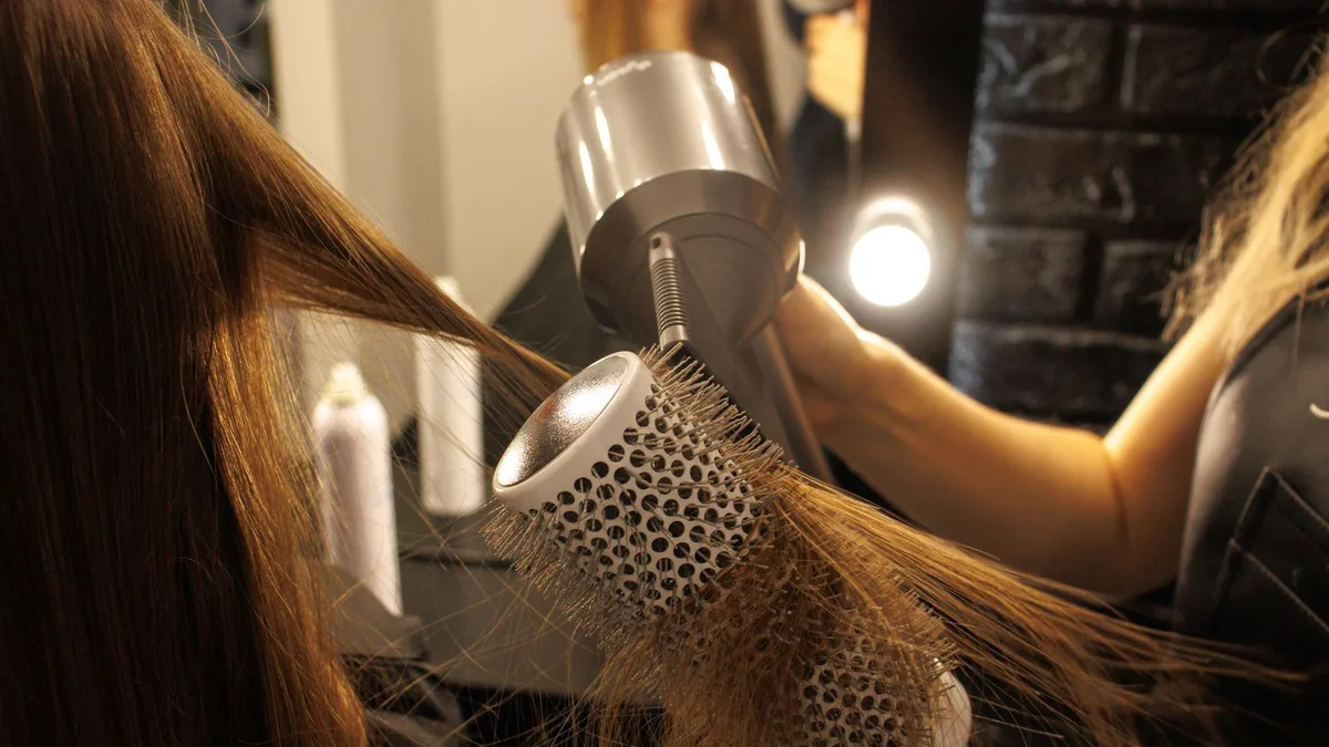 Close-up of a hairstylist drying and styling long hair with a round brush in a salon.