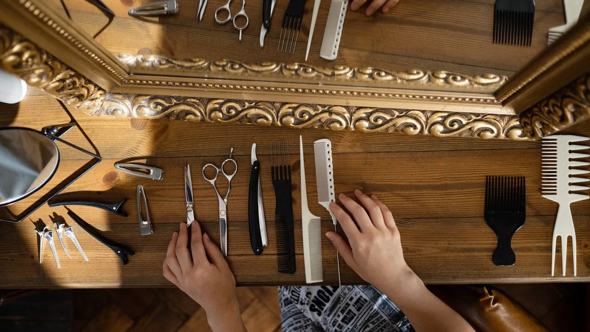 Overhead view of hair styling tools on wooden table next to a mirror.